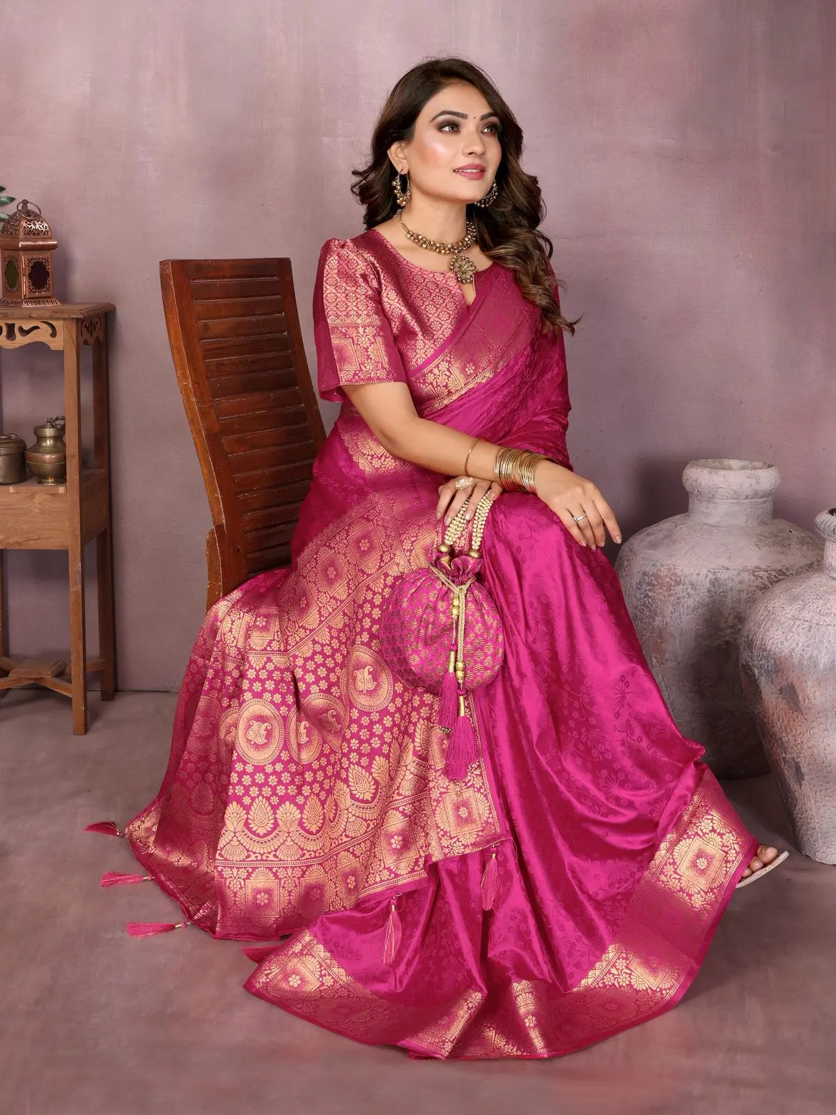 Woman in a pink saree sitting on a chair against a plain background